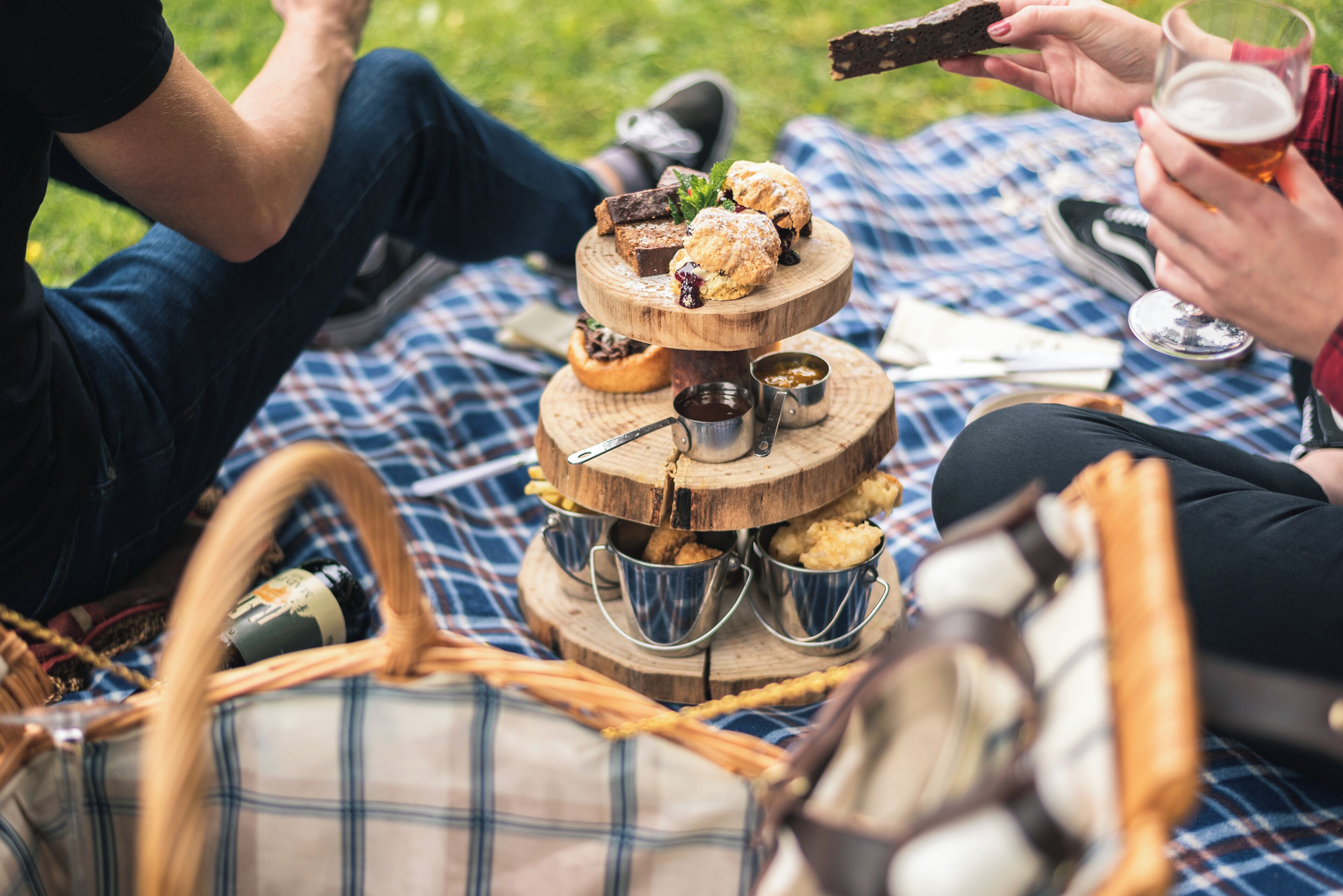 A picnic setup with a tiered wooden stand holding pastries and a drink.