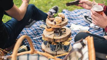 A picnic setup with a tiered wooden stand holding pastries and a drink.