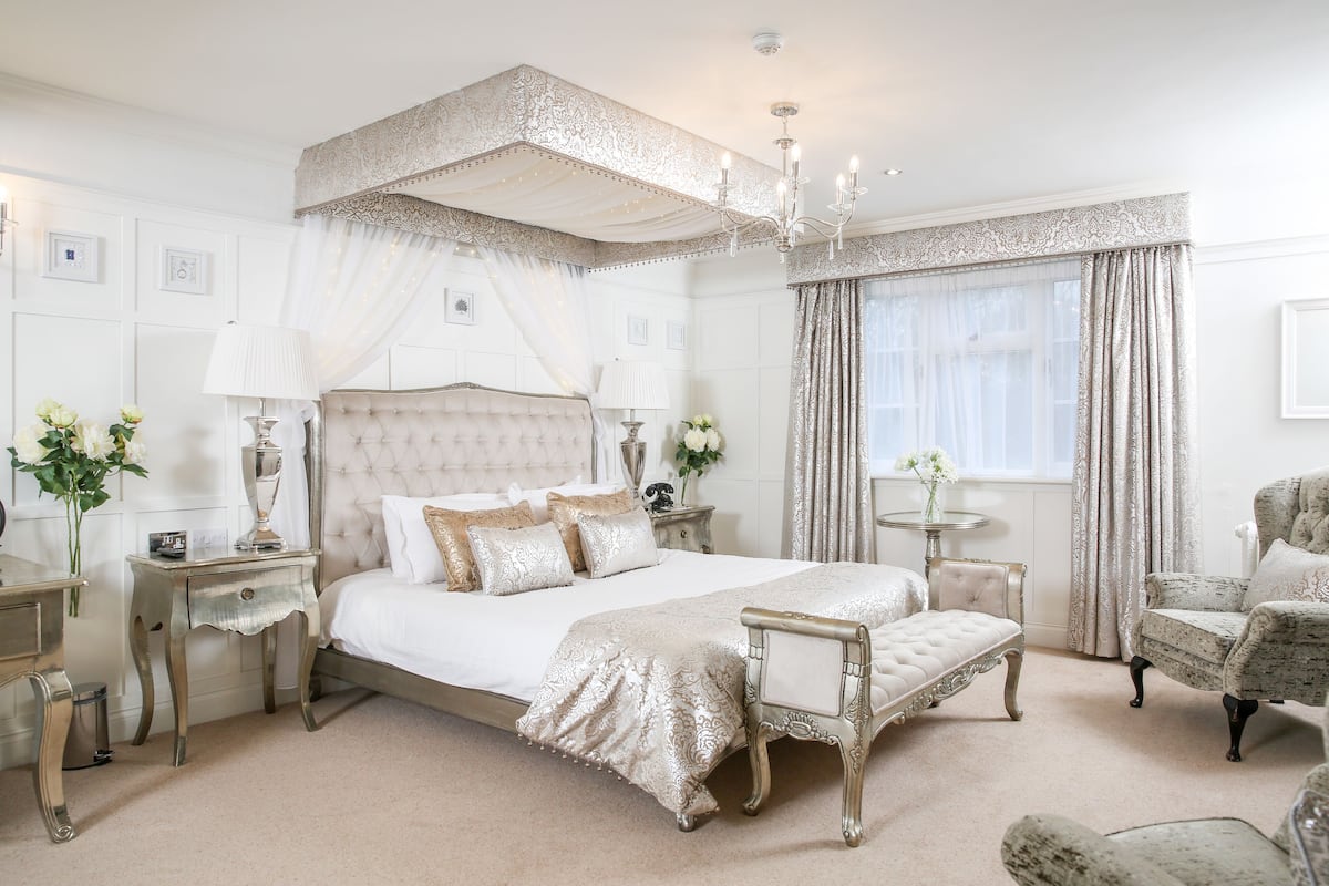 A luxurious bedroom with a large four-poster bed, a sitting area with a chaise lounge, and a classic chandelier.