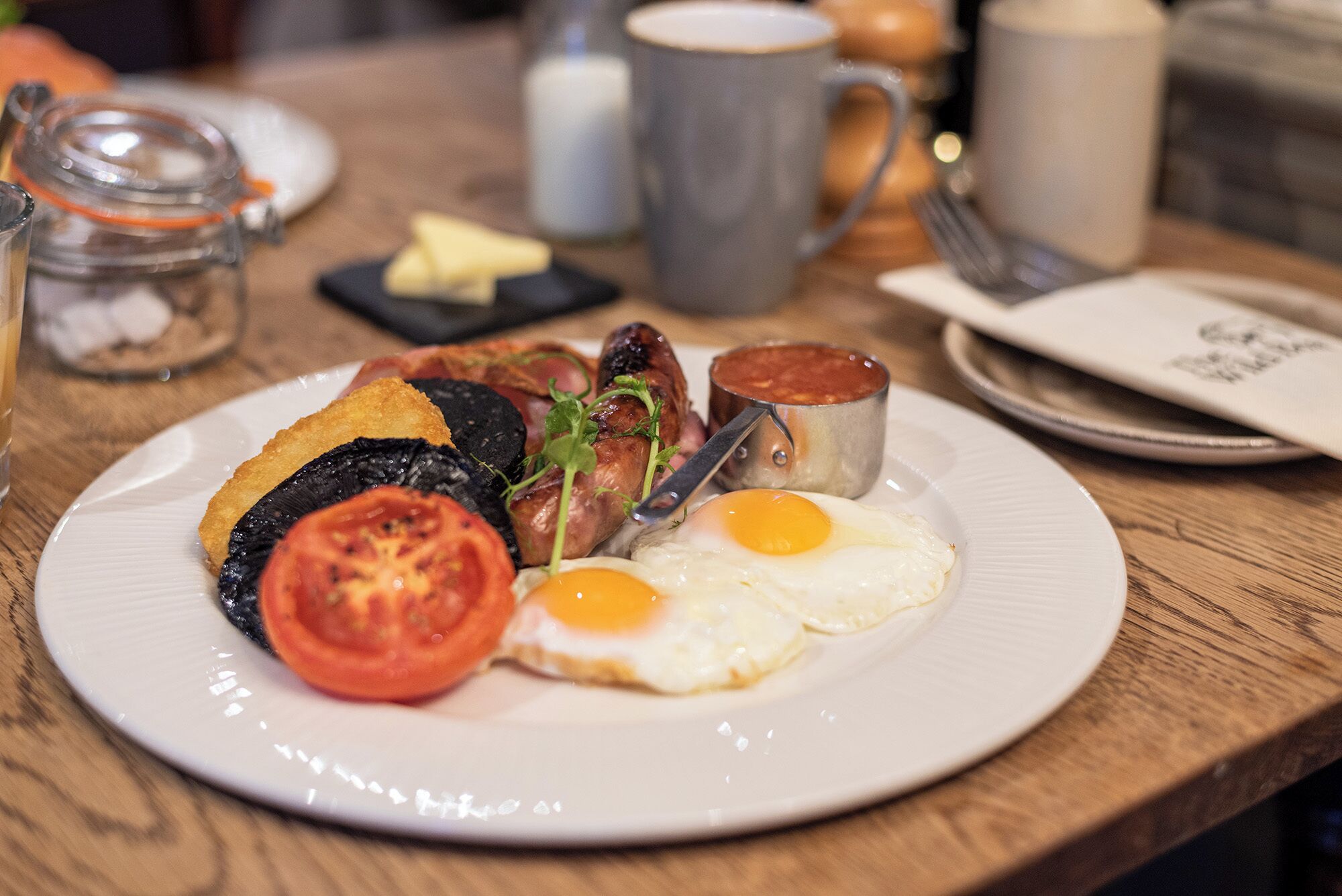 A breakfast plate with eggs, tomatoes, mushrooms, and bacon on a wooden table.