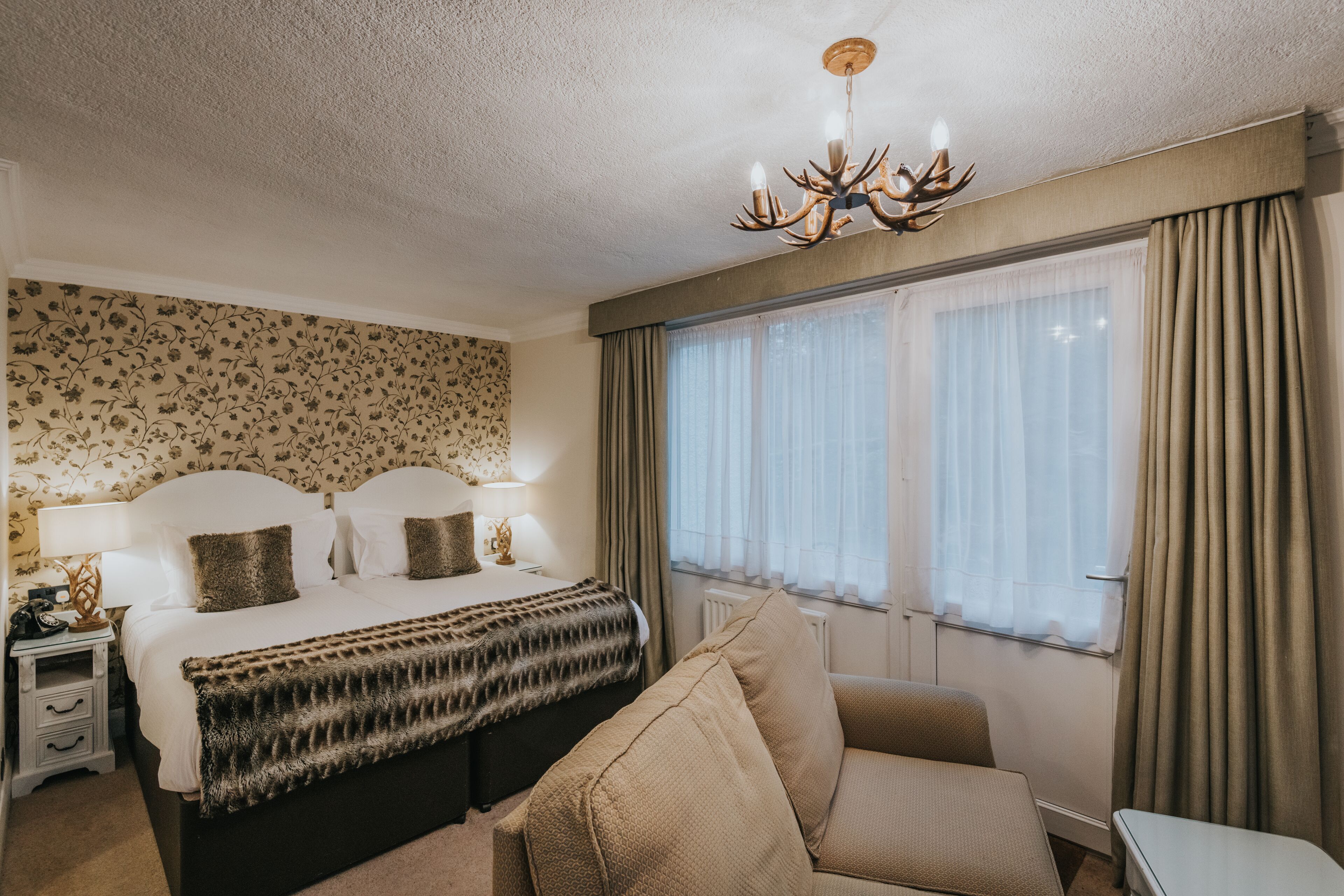 Habitación de hotel con cama, mesita de noche, lámpara y un ventanal con cortinas.