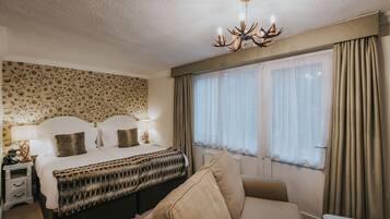 Habitación de hotel con cama, mesita de noche, lámpara y un ventanal con cortinas.