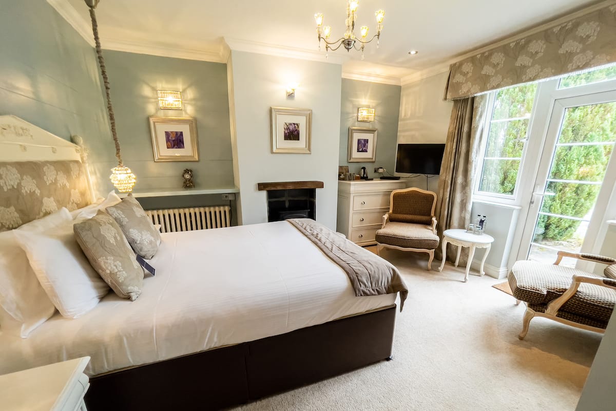 A bedroom with a large bed, a dresser, a chair, a television, and a fireplace.