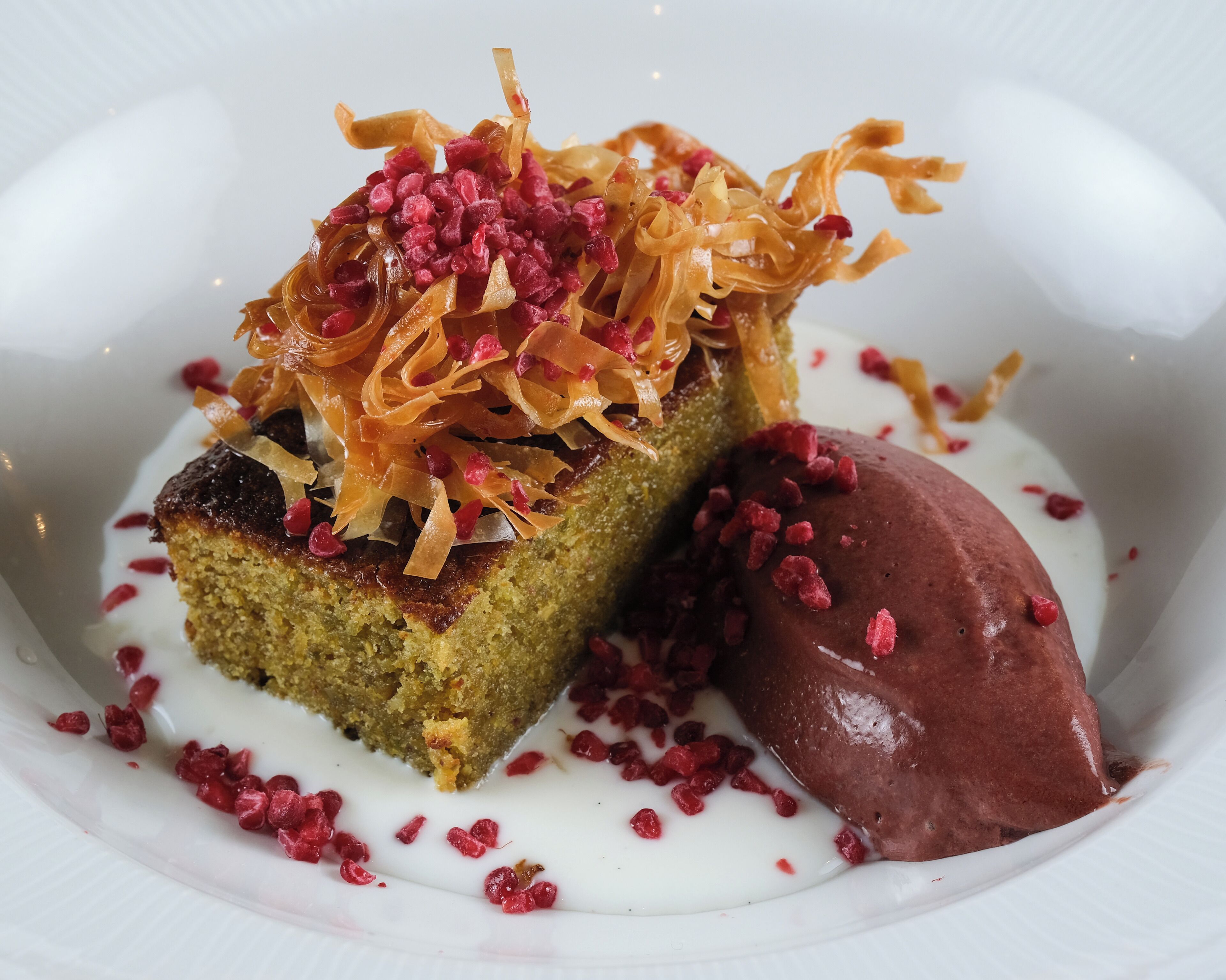 A dessert with a piece of cake topped with shredded orange and red fruit, served with a scoop of chocolate ice cream and drizzled with white sauce.