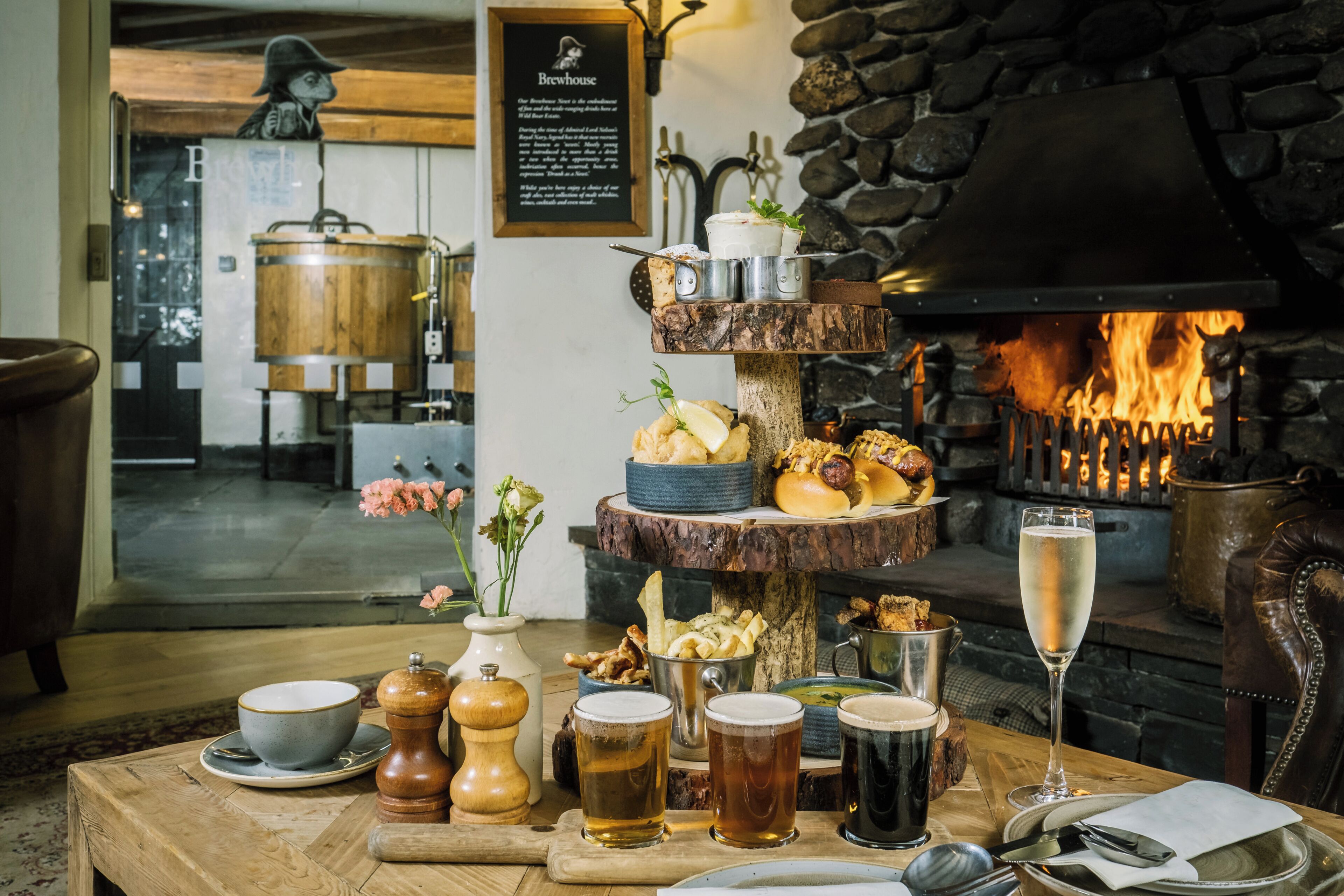 A wooden table with a variety of food items, drinks, and a fireplace in the background.