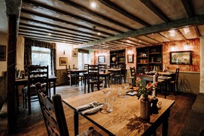 A rustic dining area with wooden tables and chairs, a globe, bookshelves, and a large window with curtains. - Wild Boar Estate (Windermere)