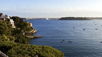 Udsigt over kysten med både på vandet, en bro og bygninger ved stranden.
