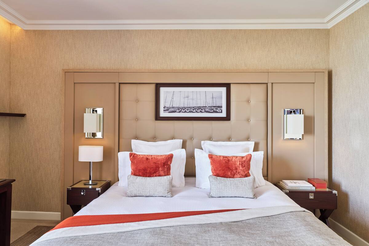 A hotel room with a large bed, two nightstands, a framed picture on the headboard, and a red throw blanket.