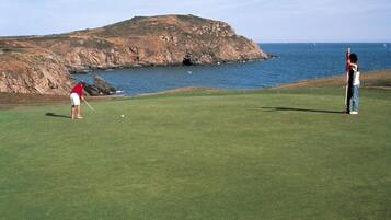 A golf course with a rocky coastline and the ocean in the background.