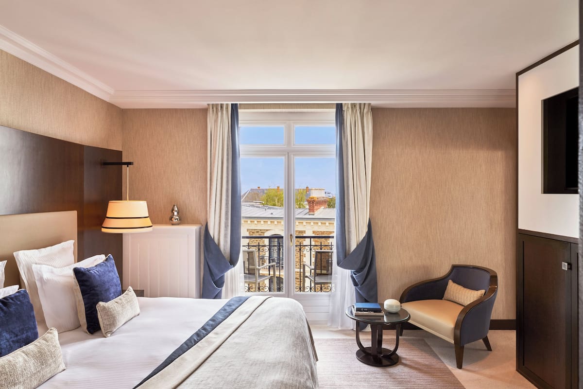 A hotel room with a large bed, a chair, a small table, and a TV.