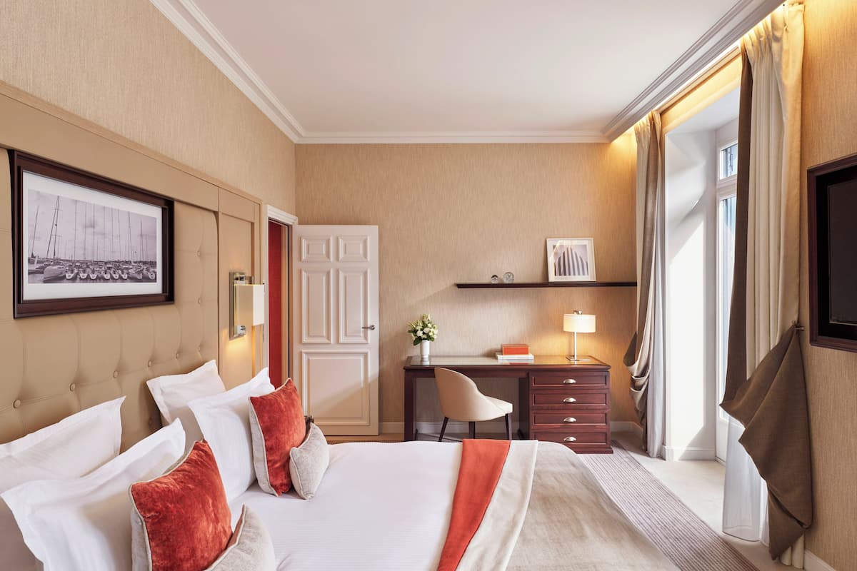 A hotel room with a bed, a desk, a chair, a TV, and a window with curtains.