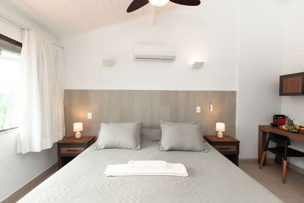 Ein Hotelzimmer mit einem großen Bett, zwei Nachttischen mit Lampen, einem Schreibtisch mit Stuhl und einer Klimaanlage an der Wand.