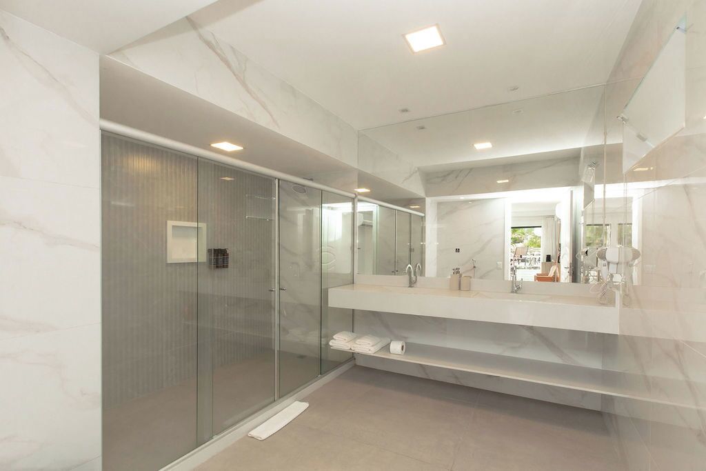 A modern bathroom with a glass shower enclosure, a large mirror, and a marble countertop.
