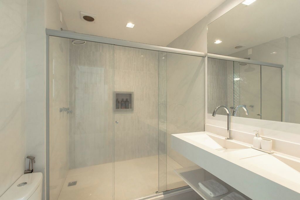 A modern bathroom with a glass-enclosed shower, a large mirror, and a white sink.