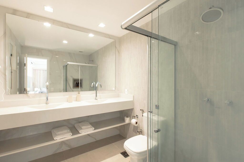 Une salle de bain moderne dotée d’une douche à parois de verre, d’un grand miroir et d’un meuble-lavabo blanc avec un évier et un porte-serviettes.