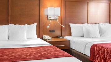 Ein Hotelzimmer mit zwei Betten, einem Holzkopfende, einem Nachttisch mit Telefon und Lampe sowie einer Wandleuchte.