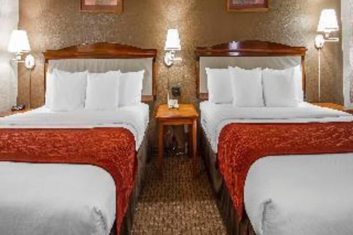 A hotel room with two beds, a small table, and two wall-mounted lamps.
