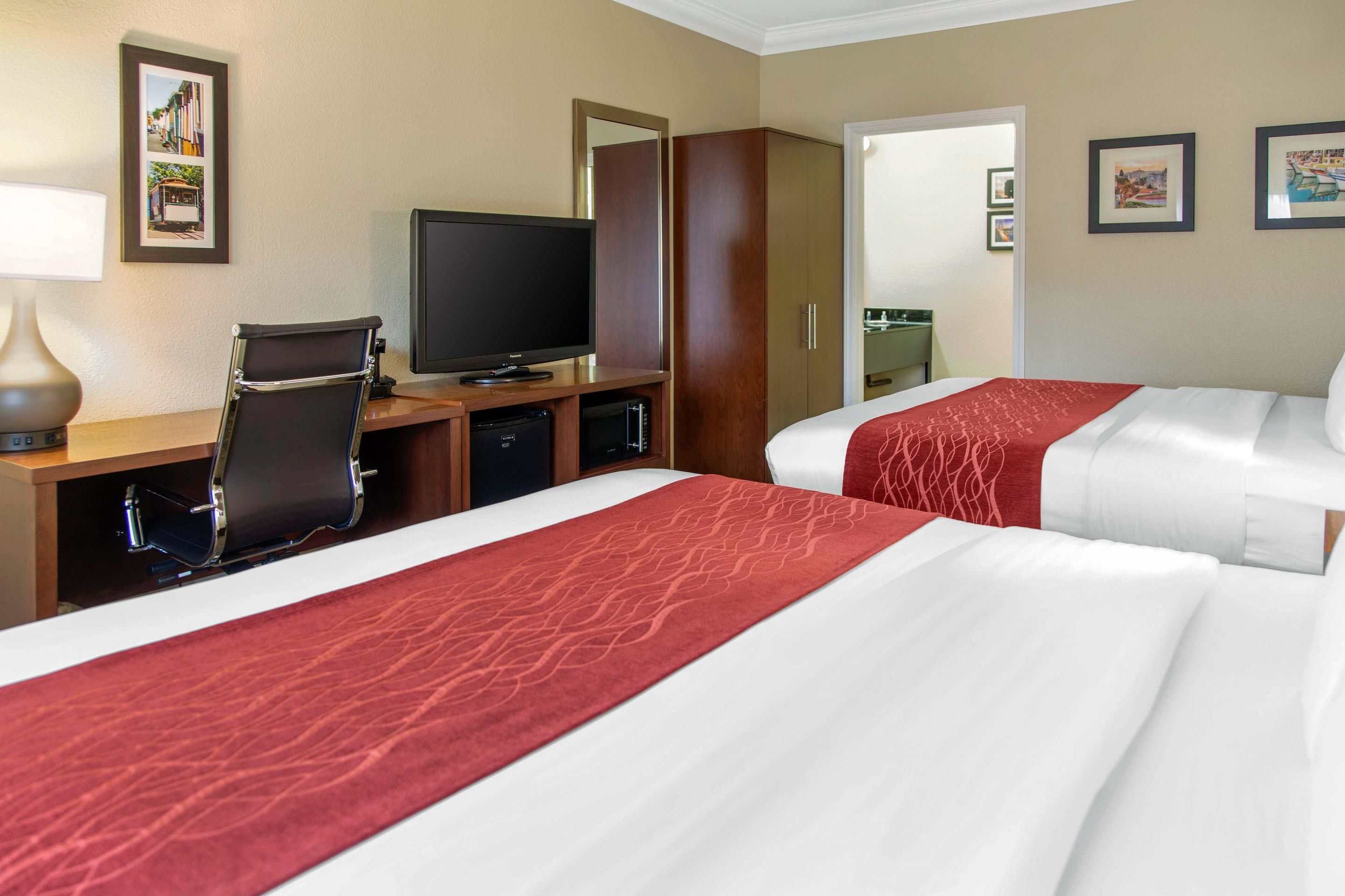 Quarto de hotel com duas camas, uma escrivaninha, televisão, espelho e guarda-roupa.