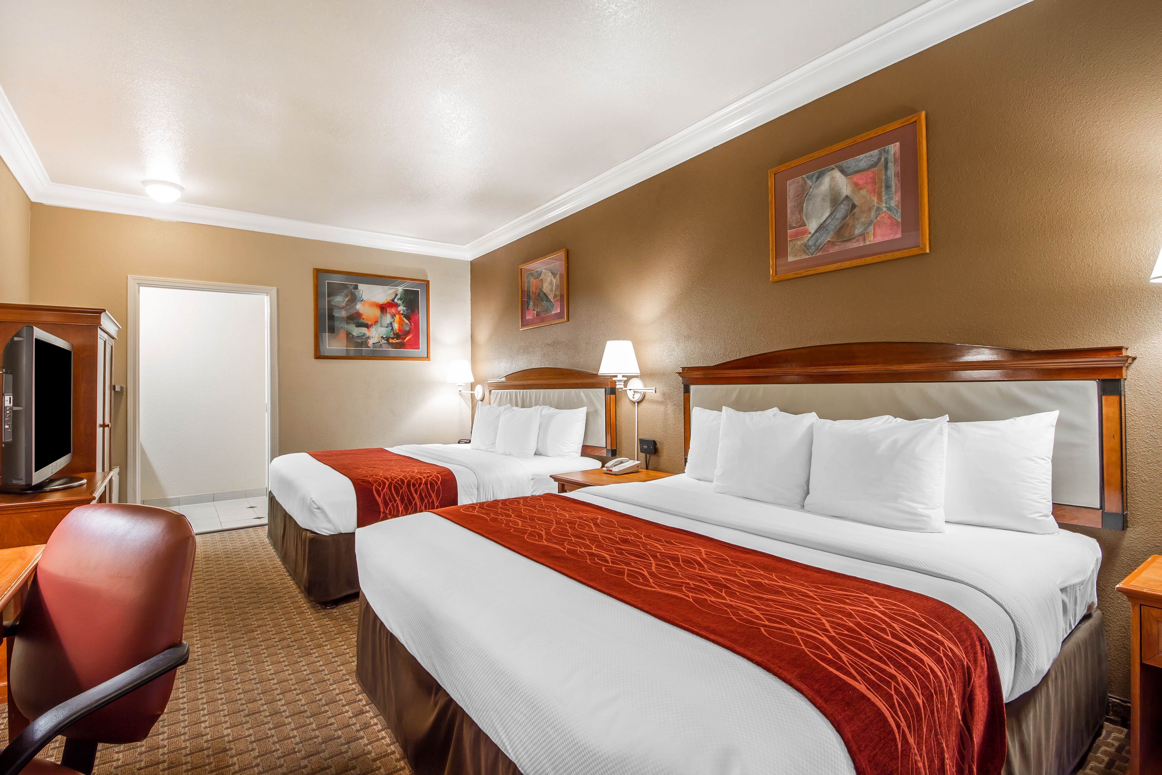 A hotel room with two beds, a TV, a desk, and artwork on the walls.