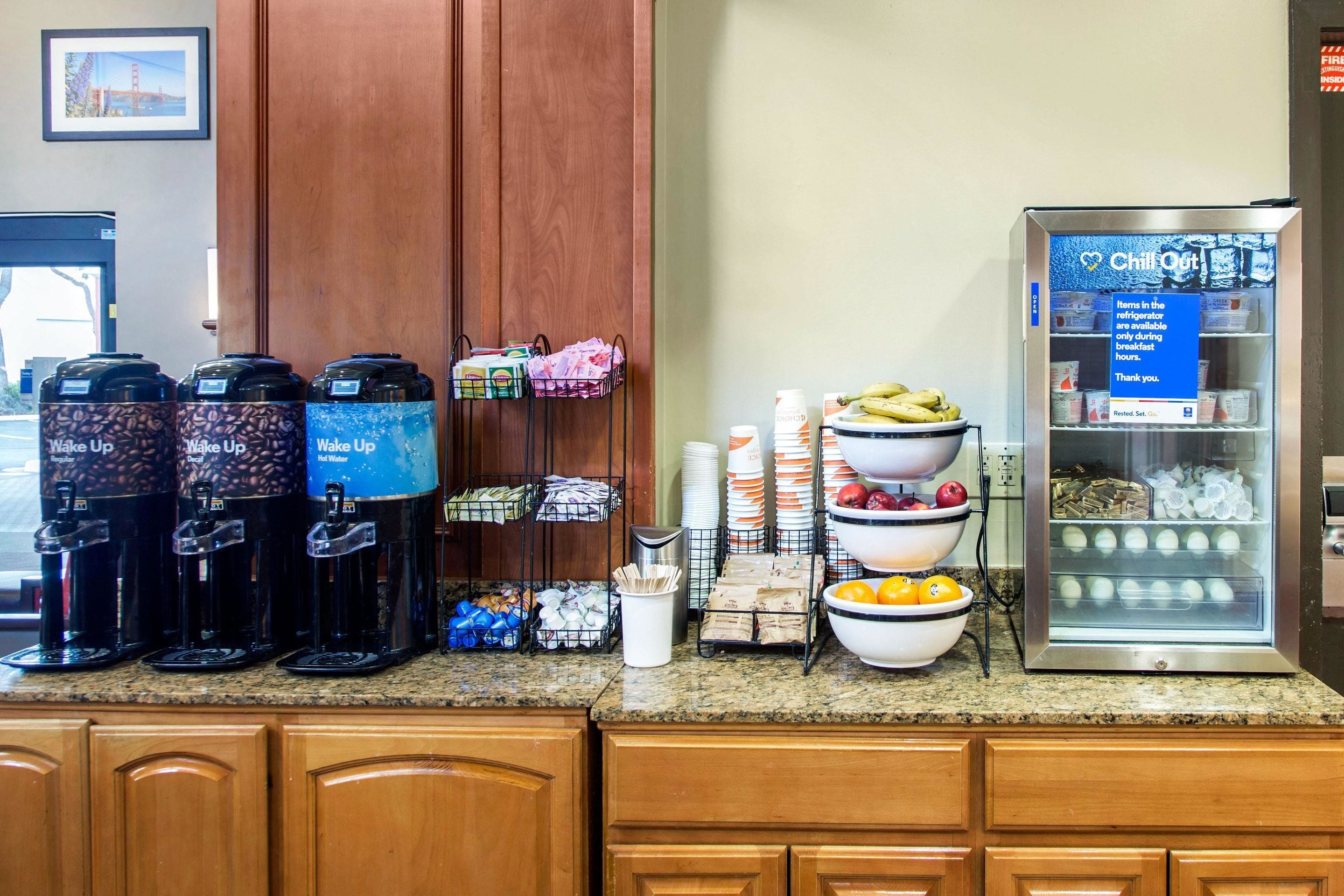 A breakfast bar with coffee makers, baskets, and a refrigerator stocked with food.