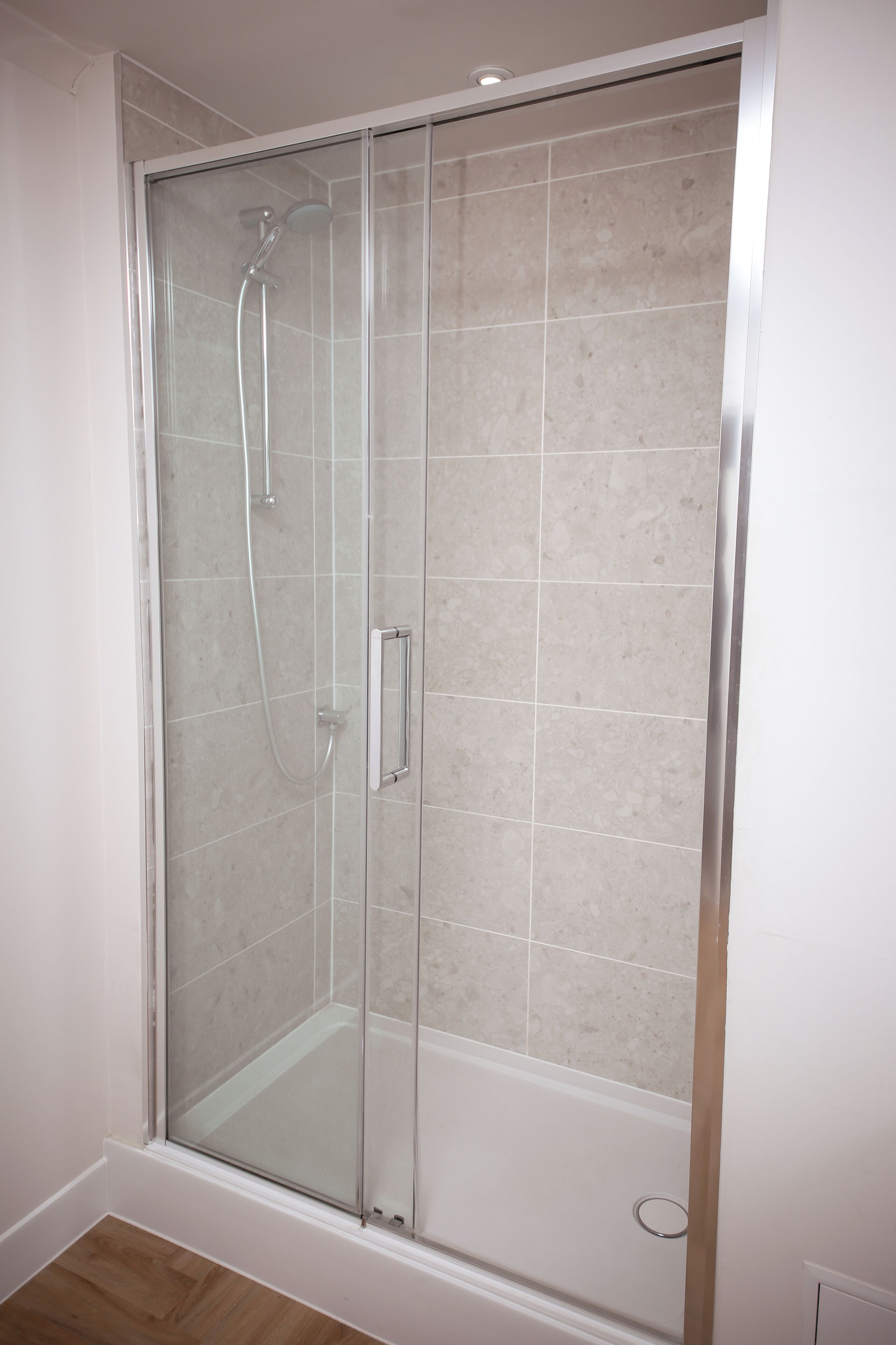 Een douche met glazen wanden, een betegelde muur en een houten vloer.