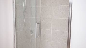 Een douche met glazen wanden, een betegelde muur en een houten vloer.