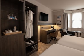 Habitación de hotel con cama, escritorio, silla, armario, televisión y ventana con cortinas.