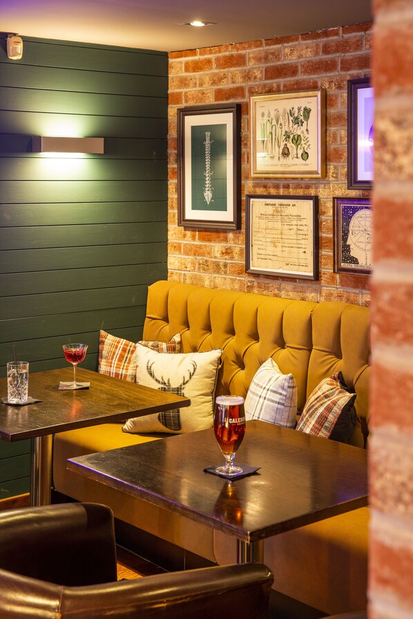 Un restaurante acogedor con pared de ladrillo, ilustraciones botánicas enmarcadas y un banco amarillo acolchado.