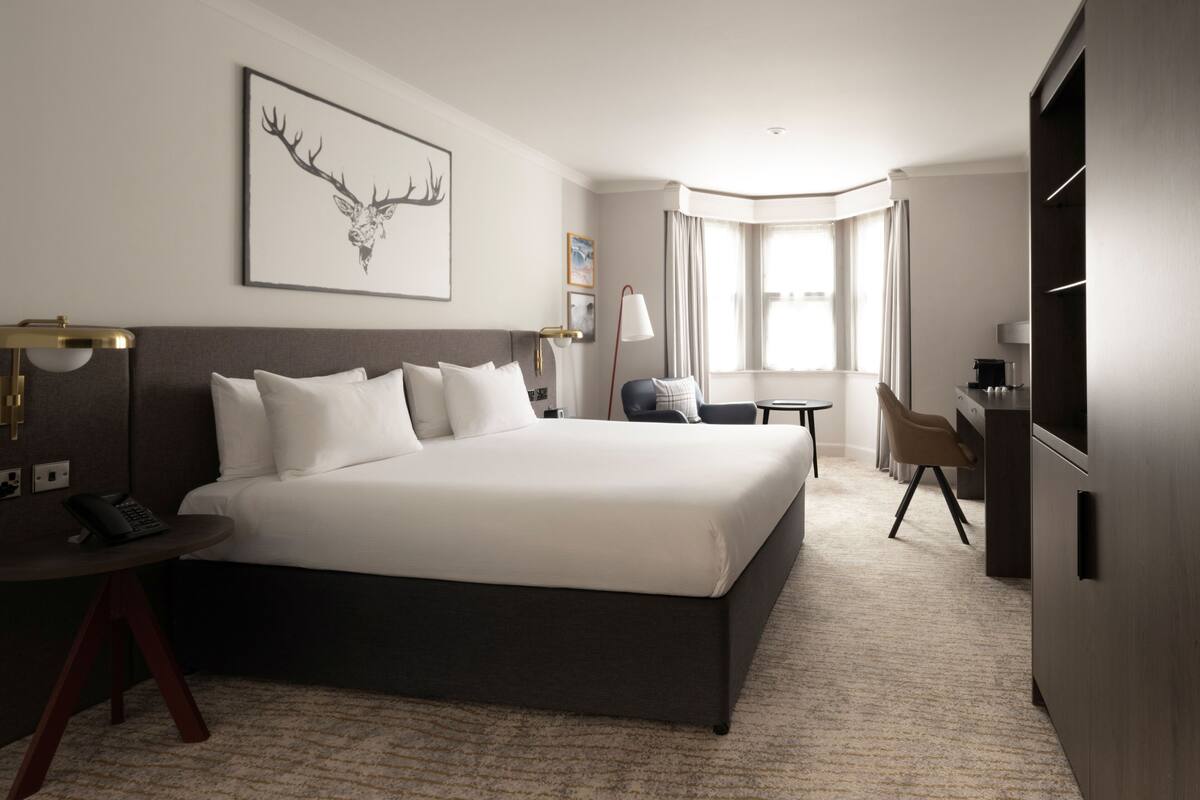 Een hotelkamer met een groot bed, een bureau, een stoel, een lamp en een raam met gordijnen.