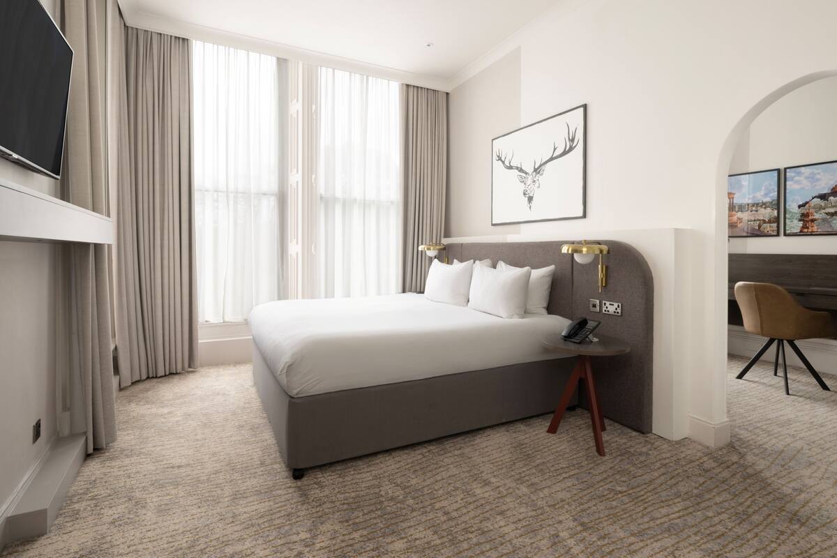 Een hotelkamer met een groot bed, een bureau met lamp, een televisie en kunstwerken aan de muur.