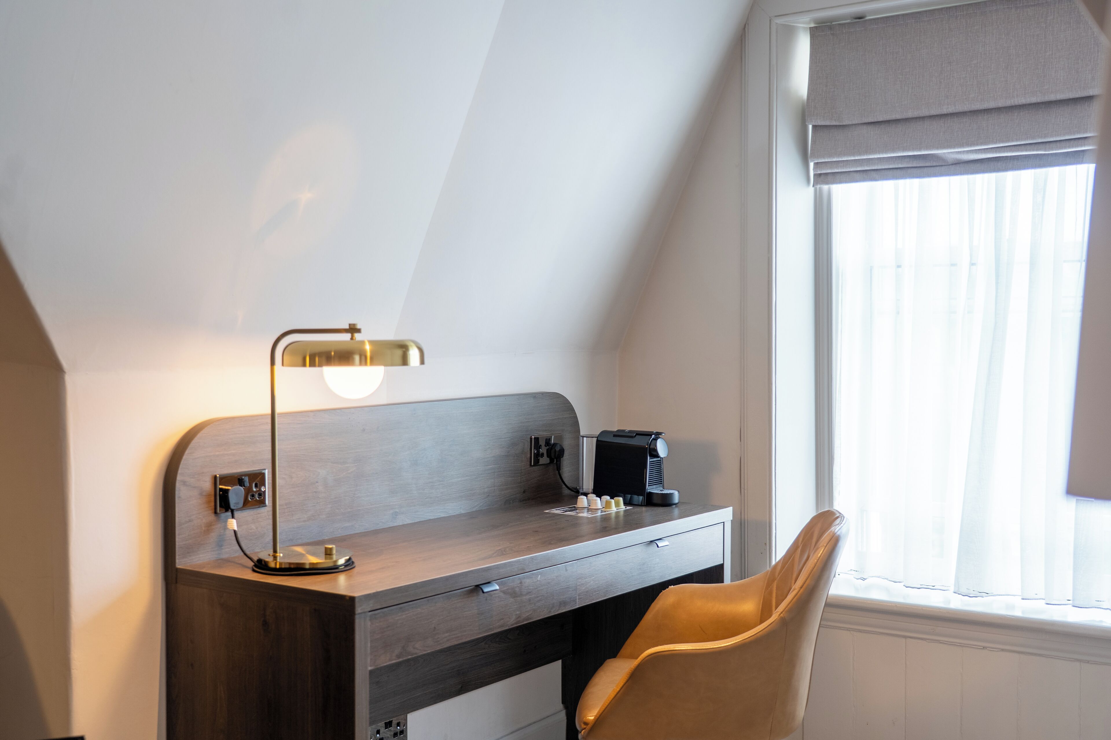 Una habitación moderna con escritorio, lámpara, silla y ventana con cortinas.