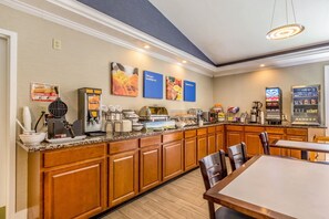 A hotel kitchen with a breakfast bar, coffee machines, and a vending machine.
