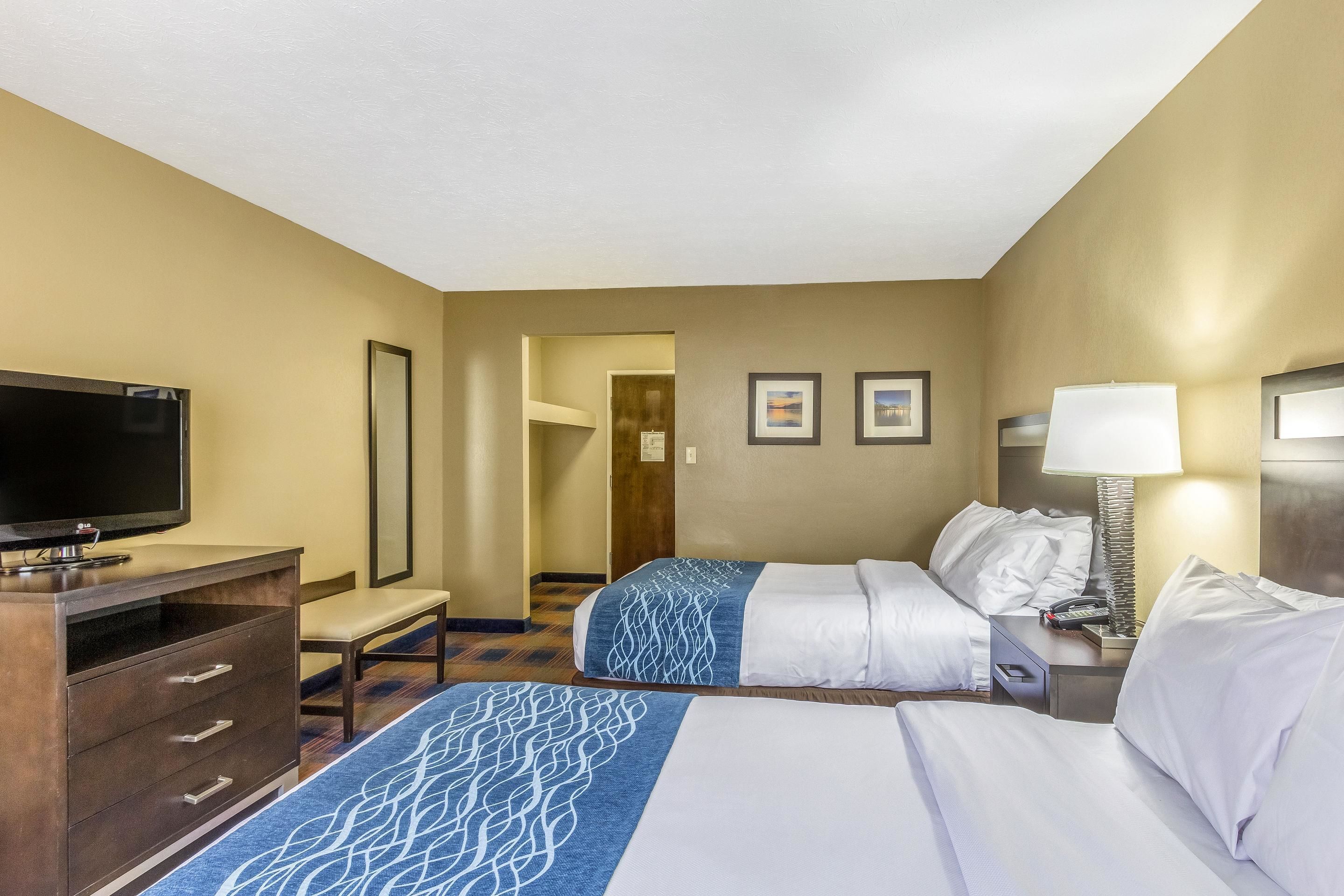 A hotel room with two beds, a desk with a television, a lamp, and a mirror.