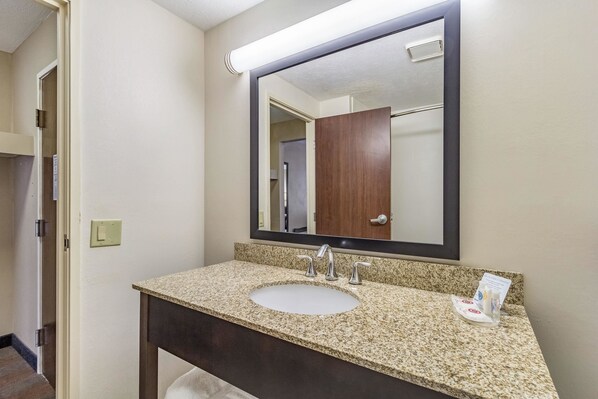 A bathroom with a granite countertop sink, a large mirror, and a wooden door in the background.