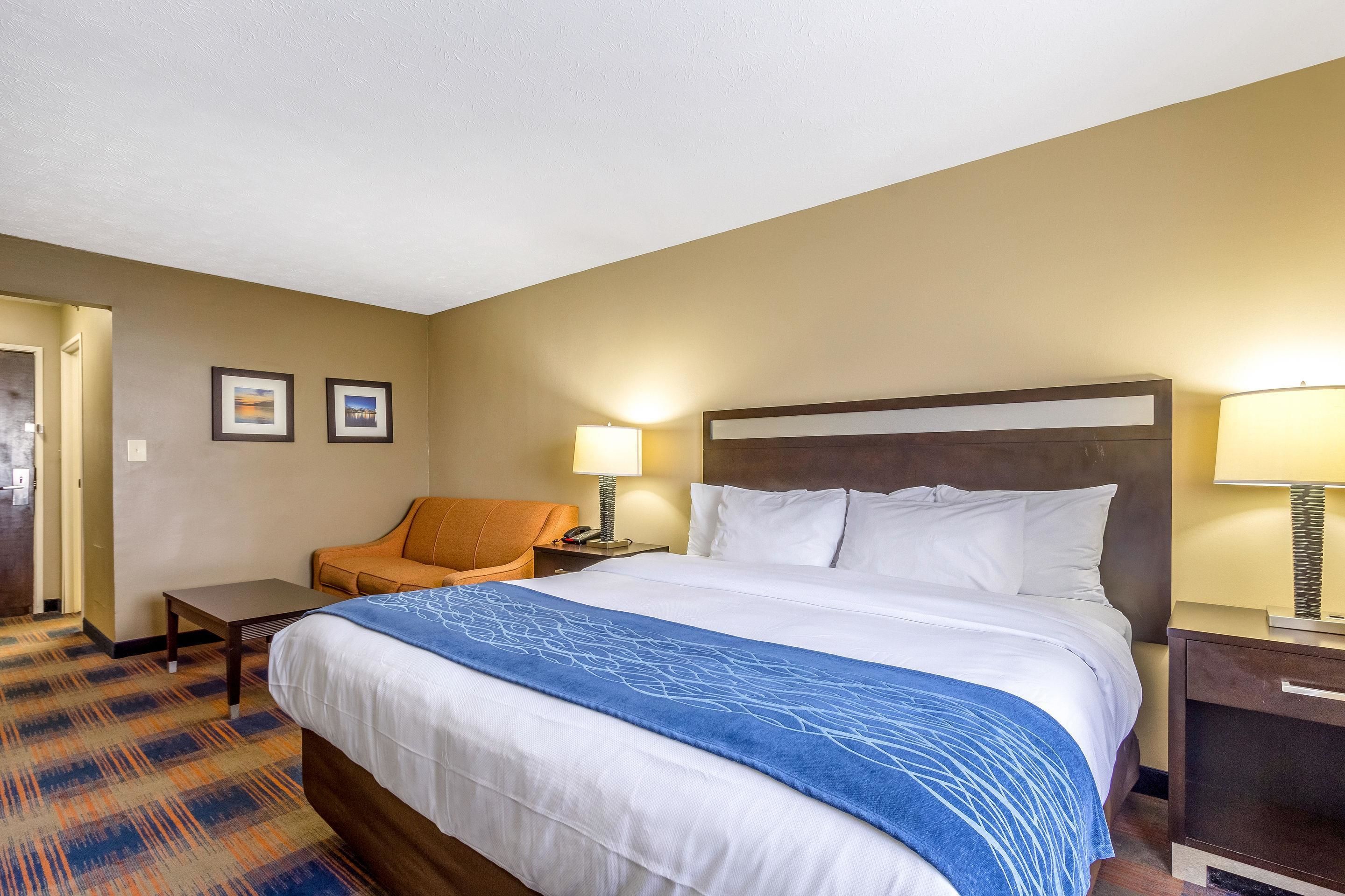 A hotel room with a large bed, a chair, two bedside tables with lamps, and a carpeted floor.