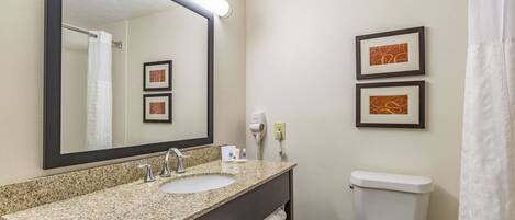 A bathroom with a granite countertop sink, a mirror, a toilet, and two framed pictures on the wall.