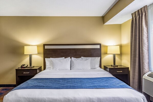 A hotel room with a large bed, two bedside tables with lamps, a headboard, and a window with curtains.
