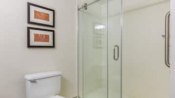 A bathroom with a glass-enclosed shower, a white toilet, and two framed pictures on the wall.