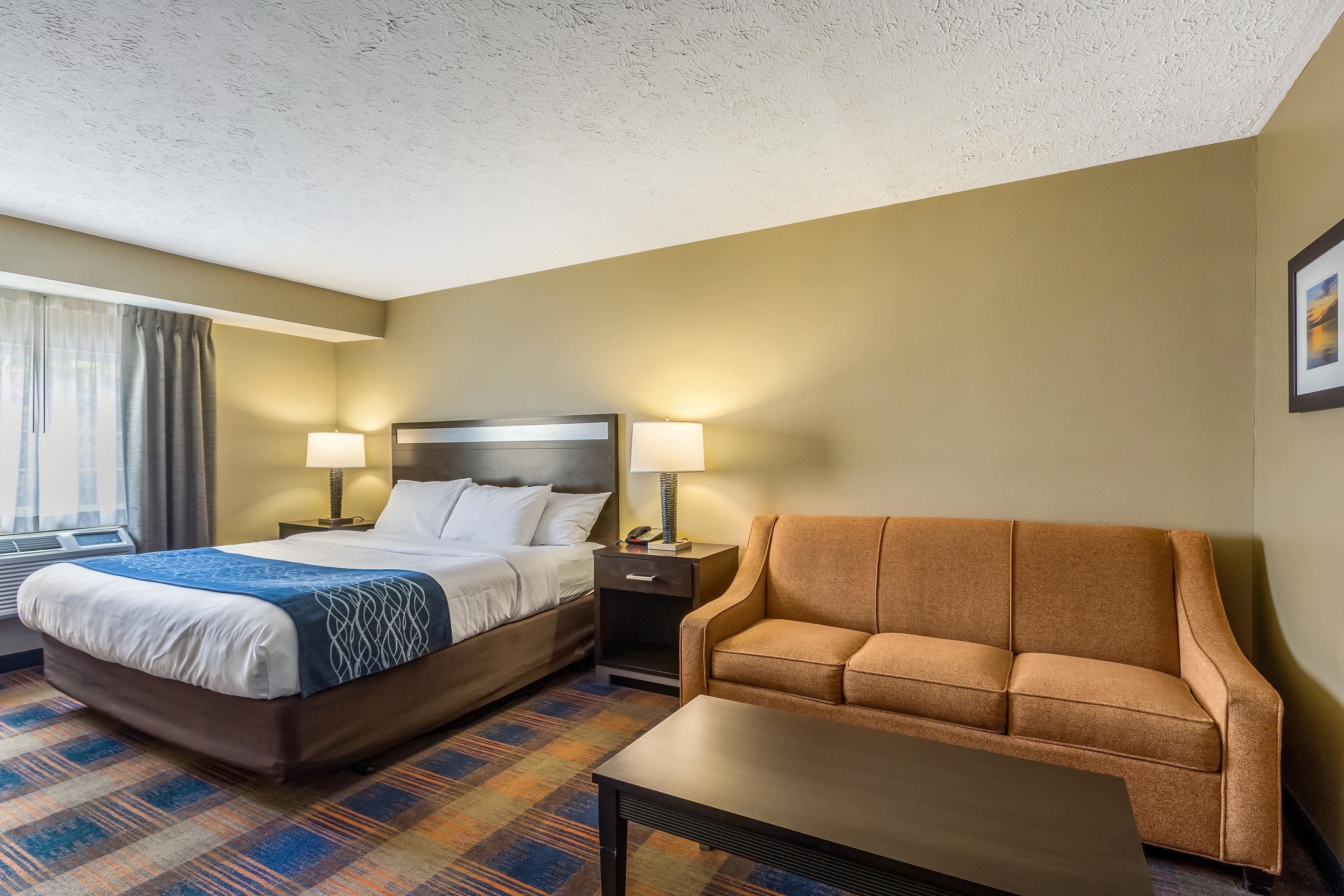 A hotel room with a bed, two bedside tables with lamps, a sofa, and a carpeted floor.