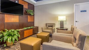 Un vestíbulo de hotel con un televisor de pantalla plana montado en la pared, una recepción y un área de estar con sillas y otomanas.