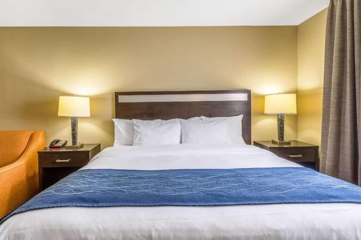 A hotel room with a bed, two bedside tables, a lamp on each table, a chair, and a curtain.