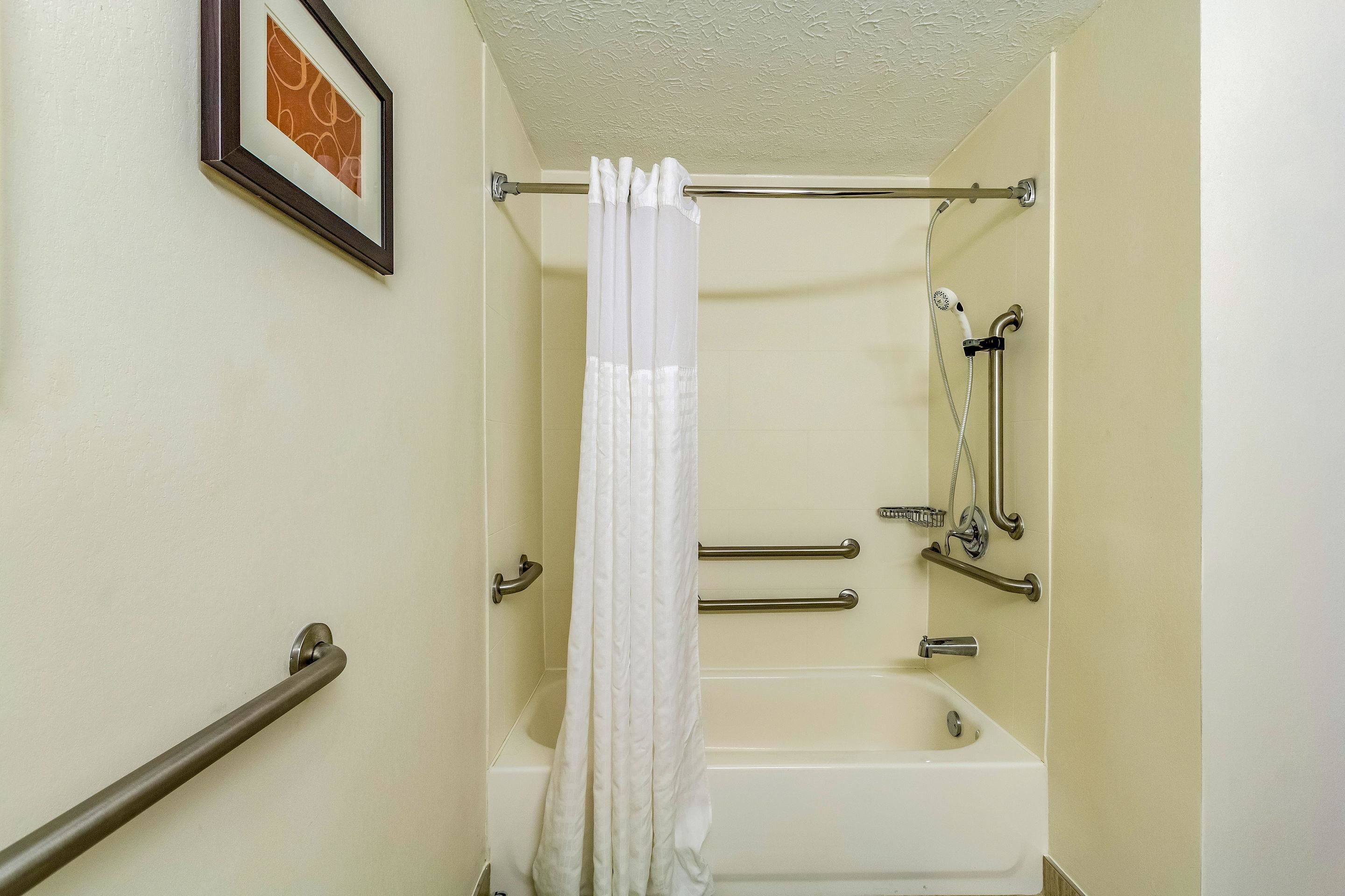 A bathroom with a bathtub, a shower, and a handrail.