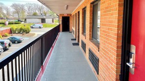 Ein überdachter Balkon im Freien mit roter Wand, schwarzem Geländer und freiem Blick auf die Straße.