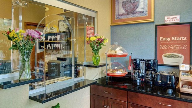 Ein Hotel-Rezeptionsbereich mit einer Kaffeestation, einem Willkommensschild und einer Frühstücksecke.