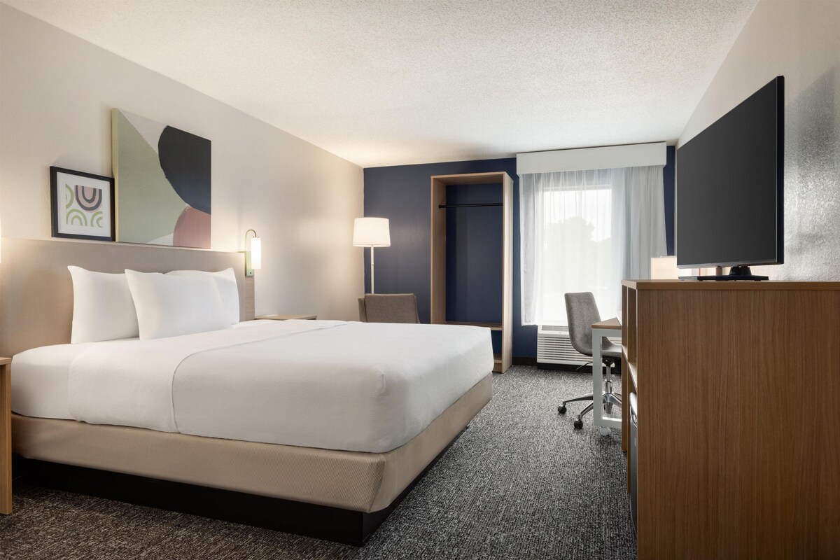 Habitación de hotel con una cama grande, un escritorio, una silla, un televisor y una puerta que da a otra habitación.