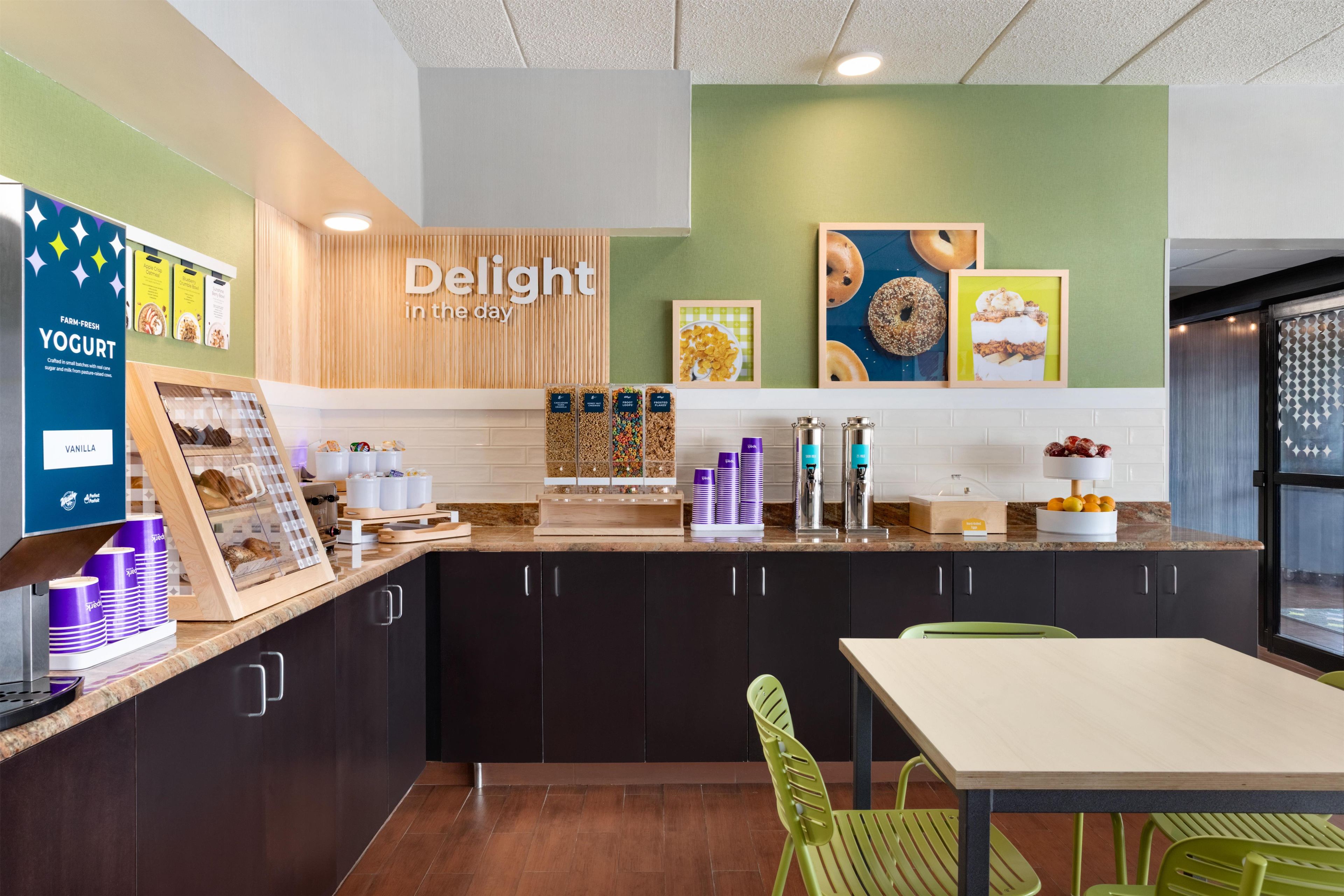 Interior de una cafetería con un mostrador que exhibe yogur y granola, un letrero que dice 'Delight in the day' y una pared con imágenes enmarcadas de comida.