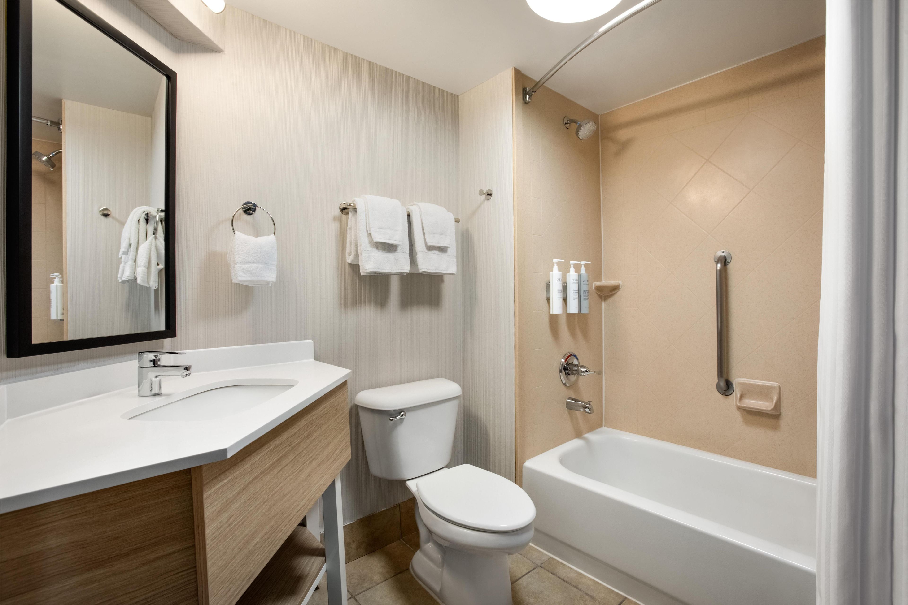 A modern bathroom with a white sink, toilet, and bathtub. There is a towel rack with towels and a mirror above the sink.