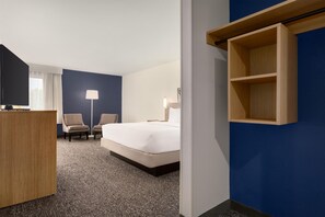 Hotellihuone, jossa on sänky, kaksi nojatuolia, työpöytä ja seinään integroitu hylly.