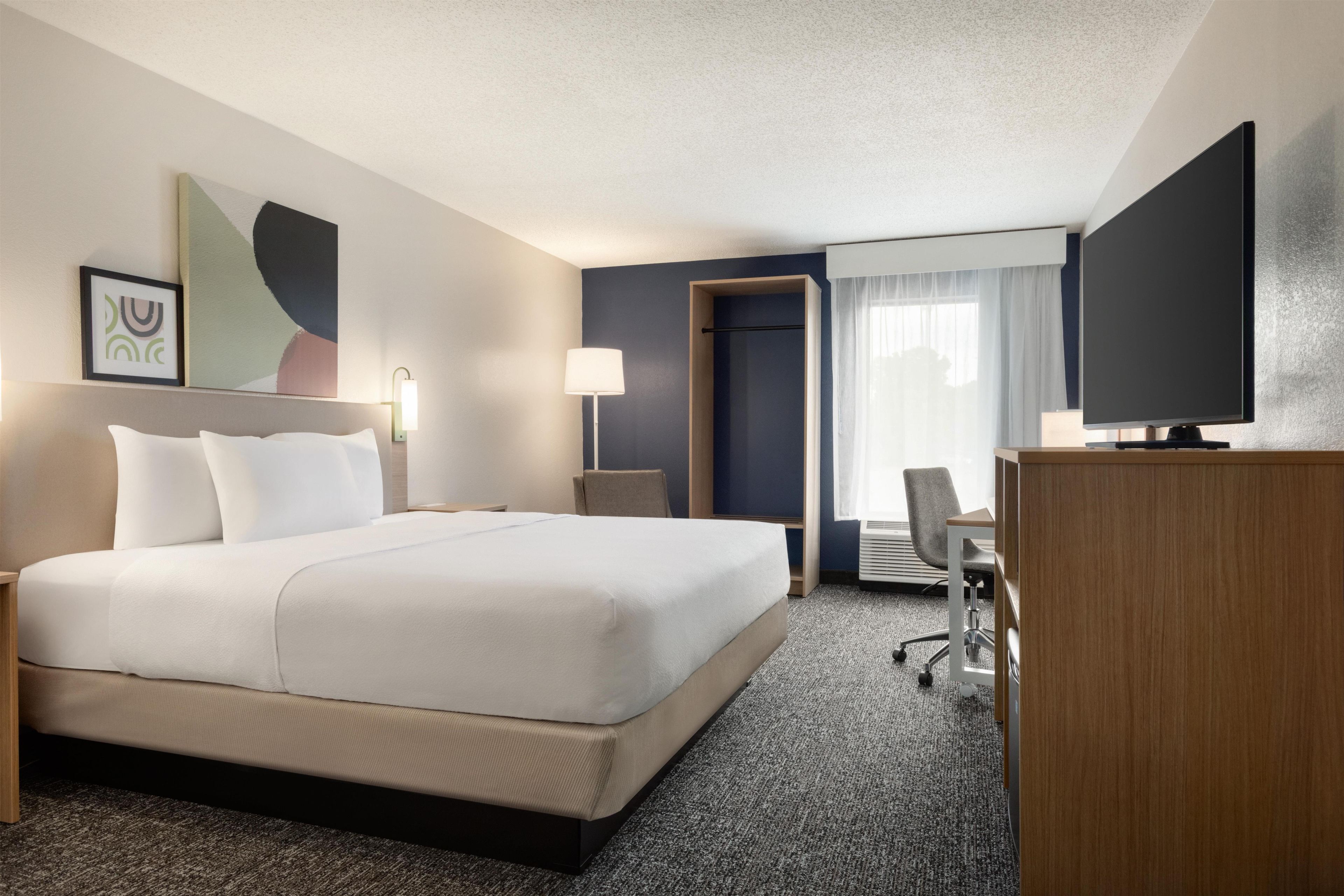 Quarto de hotel com uma cama grande, uma mesa de escritório, uma cadeira, uma televisão e uma porta que dá para outro quarto.