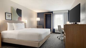 Quarto de hotel com uma cama grande, uma mesa de escritório, uma cadeira, uma televisão e uma porta que dá para outro quarto.